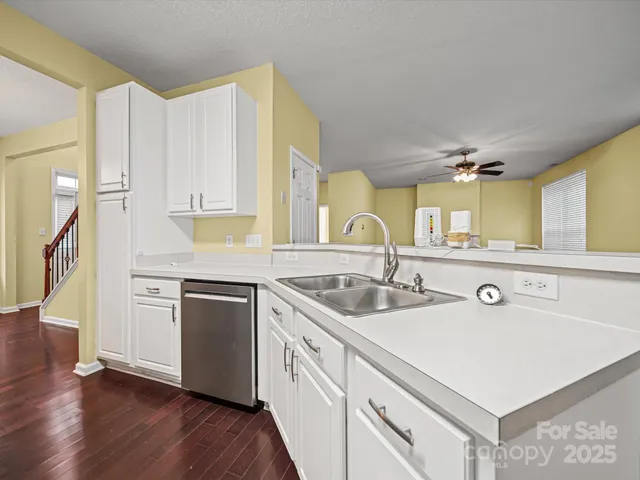 a white kitchen with a sink and dishwasher a stove top oven with wooden floor