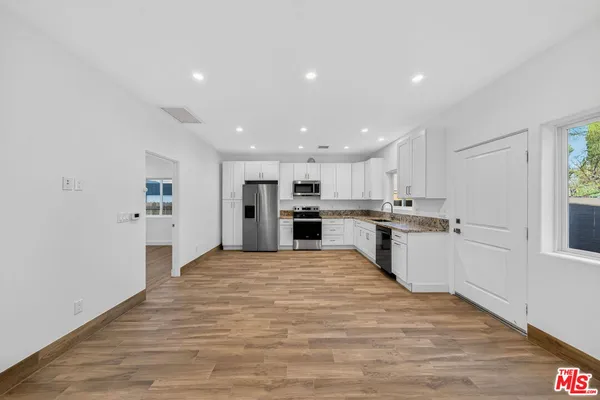 a large white kitchen with kitchen island a sink a stove a refrigerator and white cabinets with wooden floor