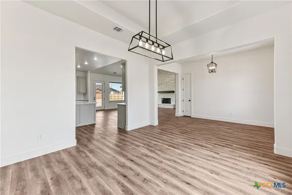 a view of an empty room and kitchen with wooden floor