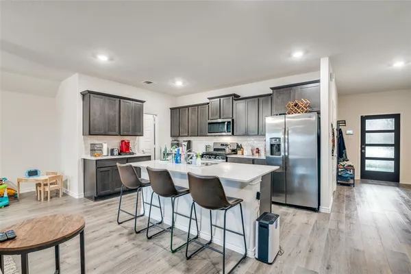 a kitchen with stainless steel appliances a refrigerator a stove a sink dishwasher and a dining table with wooden floor