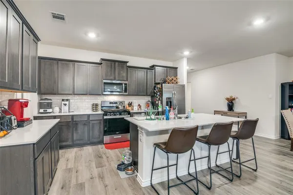 a kitchen with stainless steel appliances granite countertop a stove top oven a sink dishwasher and a refrigerator with wooden cabinets