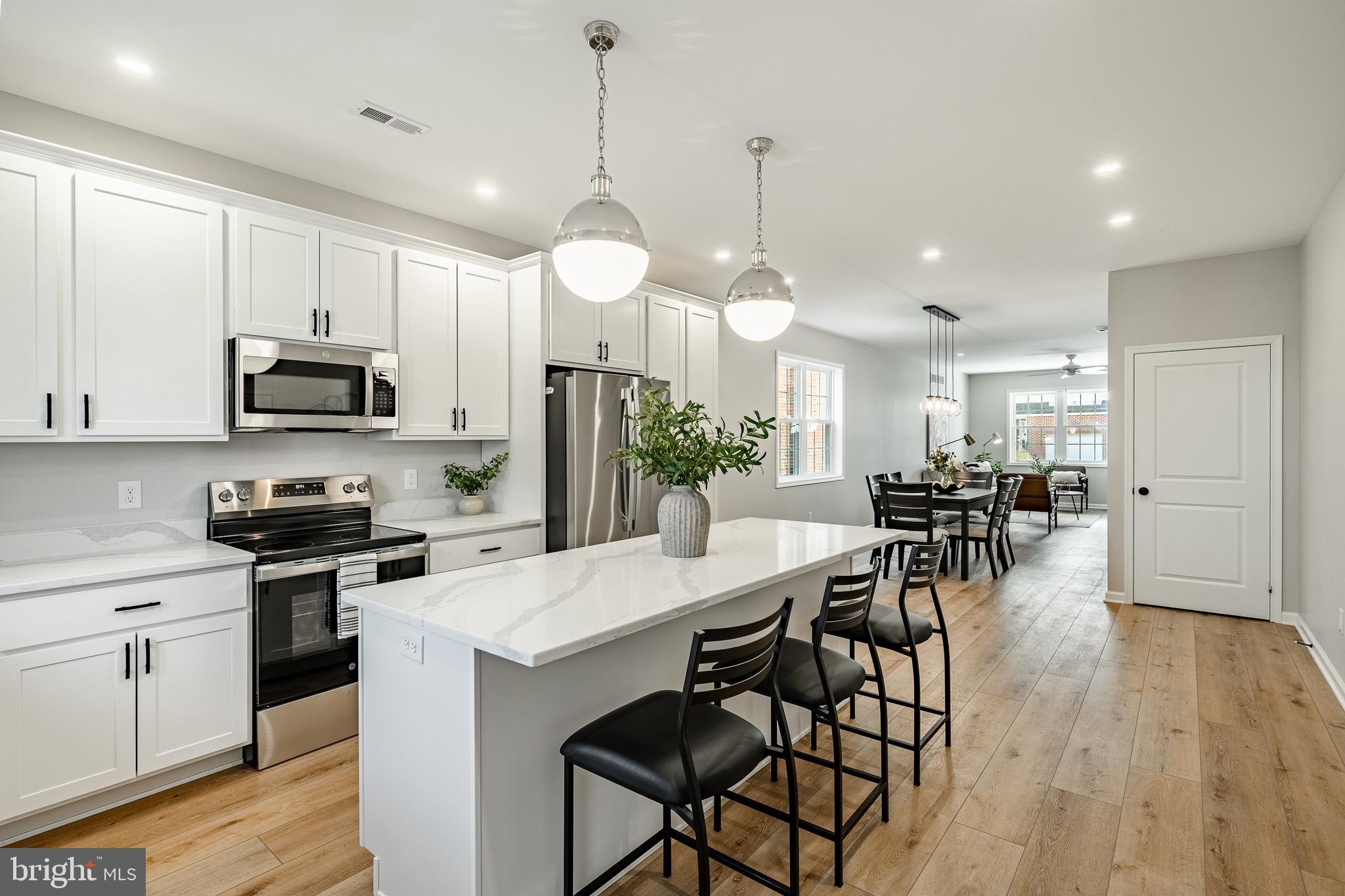 a open kitchen with stainless steel appliances granite countertop a stove a refrigerator a kitchen island a dining table and chairs with wooden floor