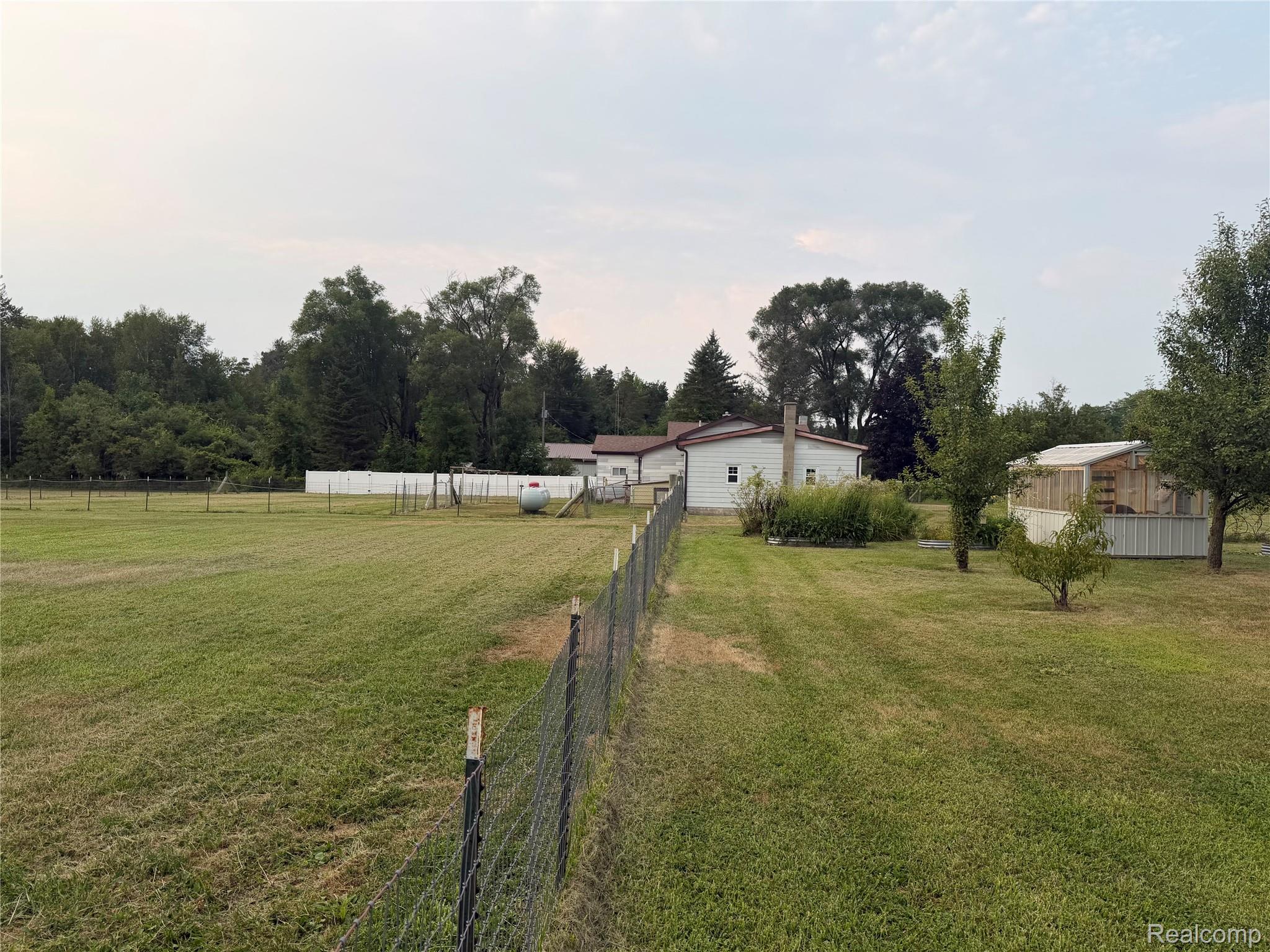2402 Mertz Road Caro, MI 48723 - Photo 23 of 26 Expansive grassy yard with perimeter fencing, a white privacy fence, and mature trees