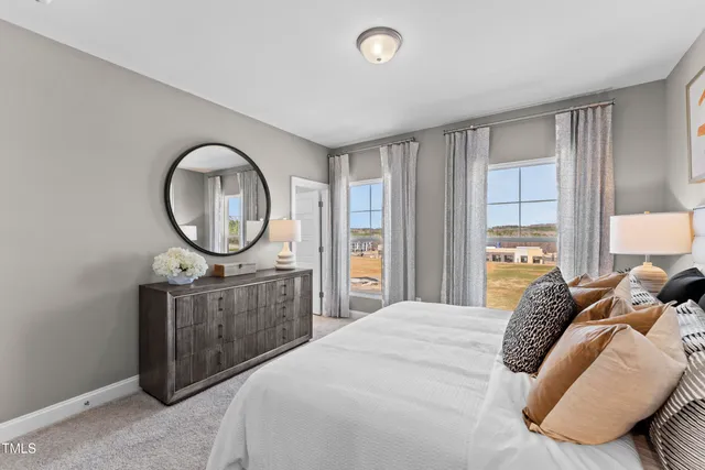 a bedroom with a bed a mirror on dresser and a large window