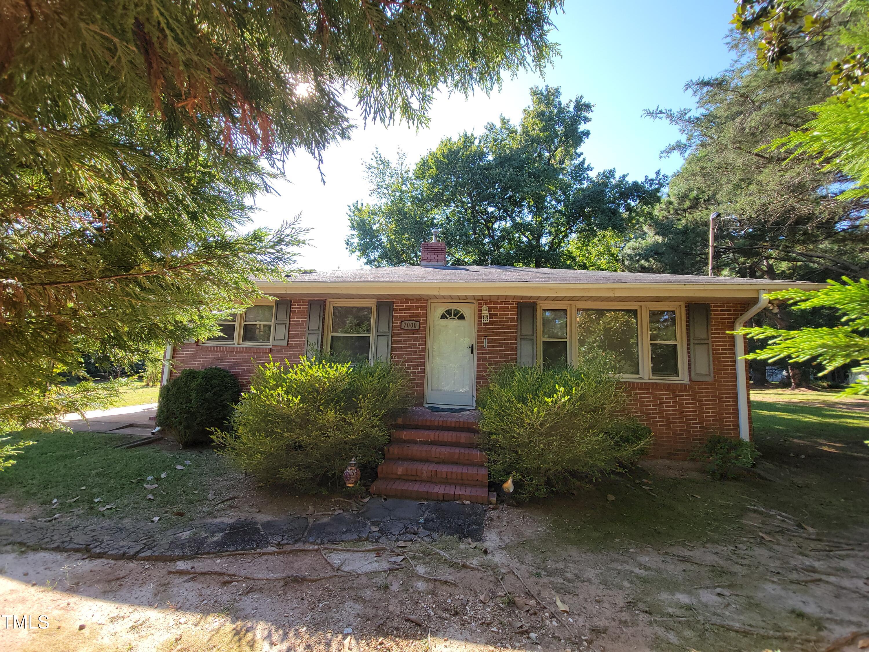 a view of a house in front of a yard with plants and large trees