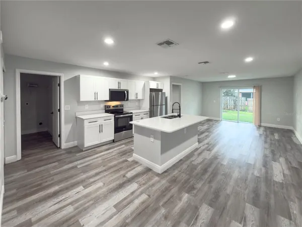 a large white room with kitchen island a sink dishwasher a stove and a refrigerator with wooden floor
