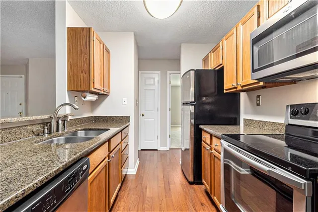 a kitchen with granite countertop stainless steel appliances a sink stove top oven and refrigerator