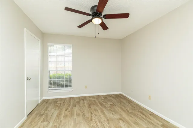 an empty room with wooden floor fan and windows