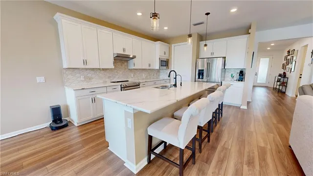 a large kitchen with stainless steel appliances a stove a sink a refrigerator and white cabinets with wooden floor