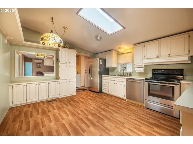 a kitchen with granite countertop a refrigerator oven a sink dishwasher and white cabinets with wooden floor