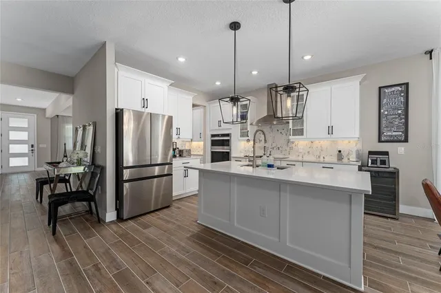 a kitchen with stainless steel appliances kitchen island granite countertop a refrigerator a sink dishwasher a oven and a dining table with wooden floor