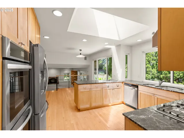 a kitchen with stainless steel appliances granite countertop a refrigerator a sink dishwasher a stove and a dining table with wooden floor