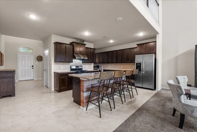 a kitchen with stainless steel appliances kitchen island granite countertop a stove a refrigerator a oven a sink with a dining table and chairs