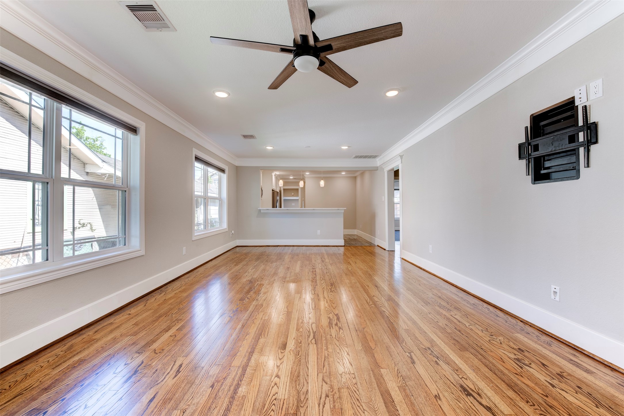 109 Dresden Street Houston, TX 77012 - Photo 11 of 43 This photo showcases a spacious, light-filled living area with hardwood floors, neutral walls, and a ceiling fan. Large windows provide ample natural light, and the room features an open layout leading to a kitchen area with a bar counter.