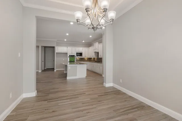 a view of an empty room and kitchen with wooden floor