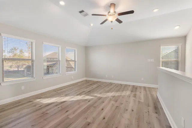 an empty room with wooden floor fan and windows