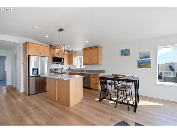 a kitchen with stainless steel appliances kitchen island granite countertop a refrigerator a stove a sink a dining table and chairs with wooden floor