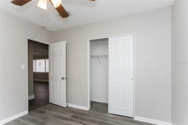 an empty room with wooden floor closet and windows
