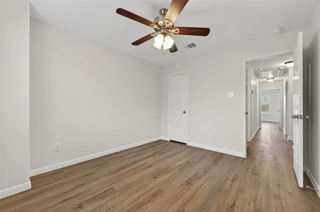 an empty room with wooden floor ceiling fan and window