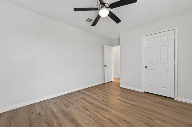an empty room with wooden floor chandelier fan and windows