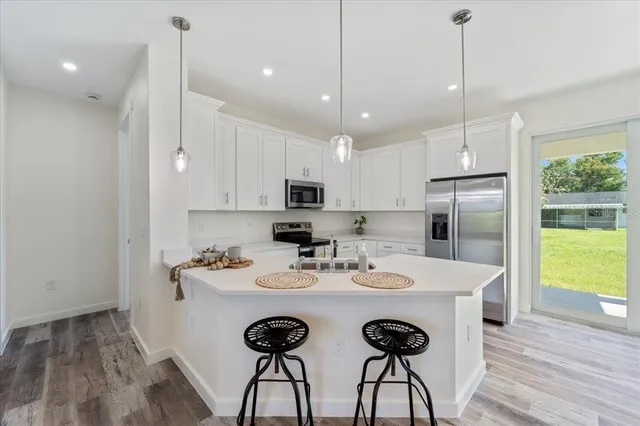 a kitchen with kitchen island a stove a refrigerator a sink and a dining table with wooden floor