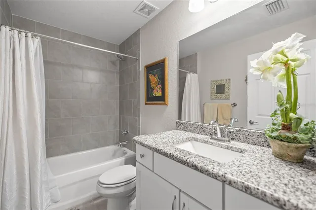 a bathroom with a granite countertop sink a toilet a mirror a vanity a bathtub and shower