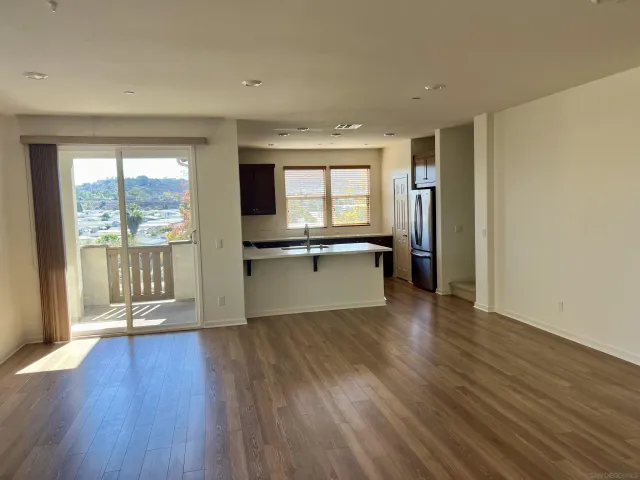 a view of a kitchen and an empty room with wooden floor and a window