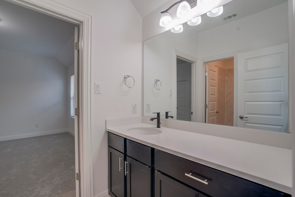 2920 Hadley Way Leander, TX 78641 - Photo 16 of 20 A sleek vanity with a wide mirror and dark cabinetry anchors this modern primary bathroom.