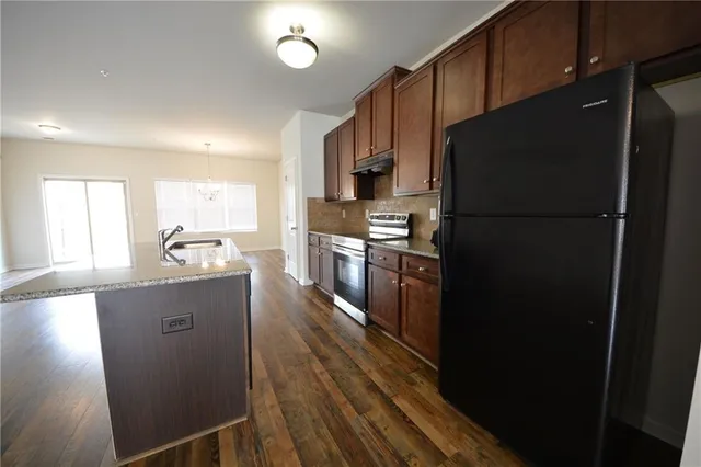 a kitchen with stainless steel appliances granite countertop a refrigerator a sink dishwasher a stove and white countertops with wooden floor