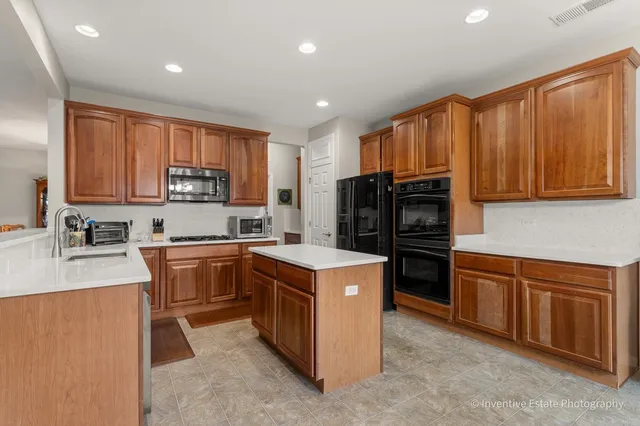 a kitchen with stainless steel appliances granite countertop a stove top oven a sink dishwasher and a refrigerator with wooden cabinets