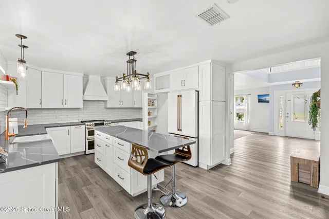 a kitchen with granite countertop a stove a sink a refrigerator and white cabinets with wooden floor