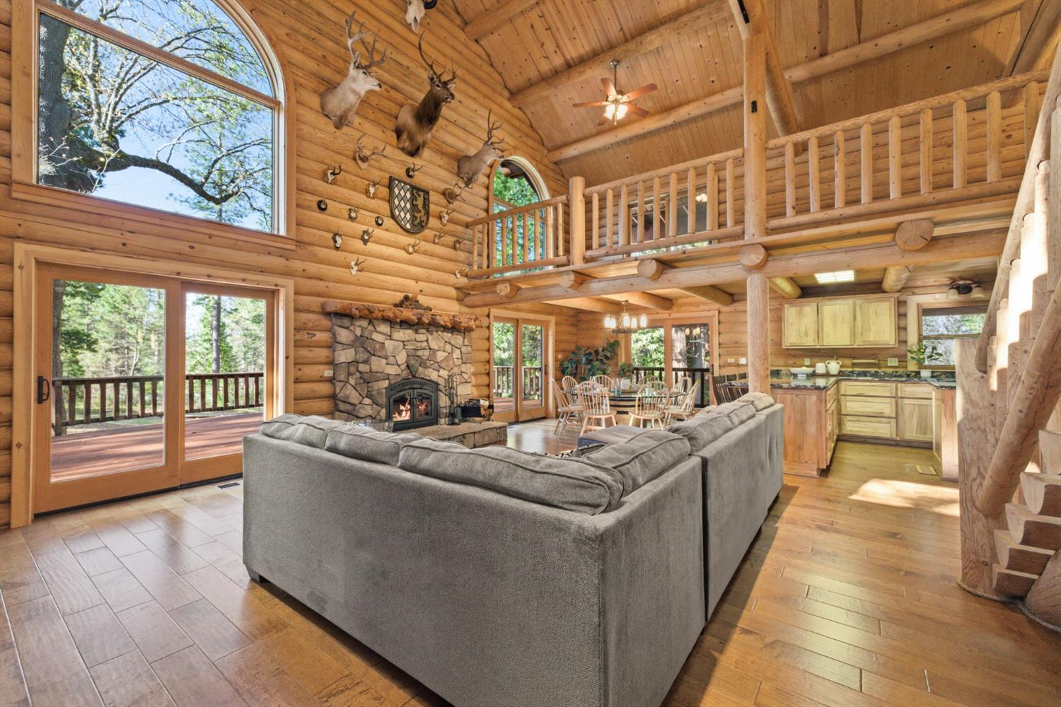 2428 Rancho Paradiso Arnold, CA 95223 - Photo 19 of 67 Soaring exposed timber trusses and arched picture windows flood the space with natural light, complemented by engineered hardwood flooring and a commanding stone fireplace that serves as the heart of the home.