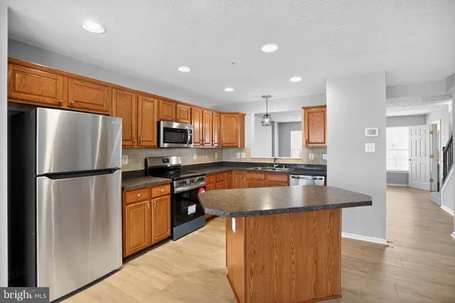 a kitchen with stainless steel appliances granite countertop a refrigerator a sink a stove a microwave a center island and a refrigerator