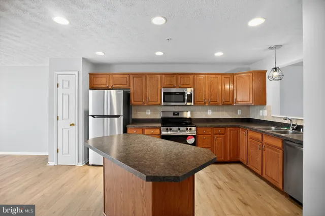 a kitchen with stainless steel appliances granite countertop a refrigerator a sink dishwasher a stove with wooden cabinets and wooden floor