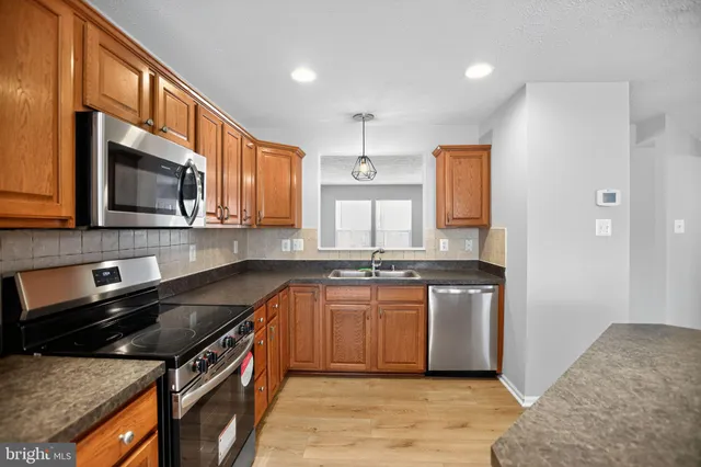 a kitchen with stainless steel appliances granite countertop a stove top oven a sink dishwasher a microwave oven and a refrigerator with wooden floor