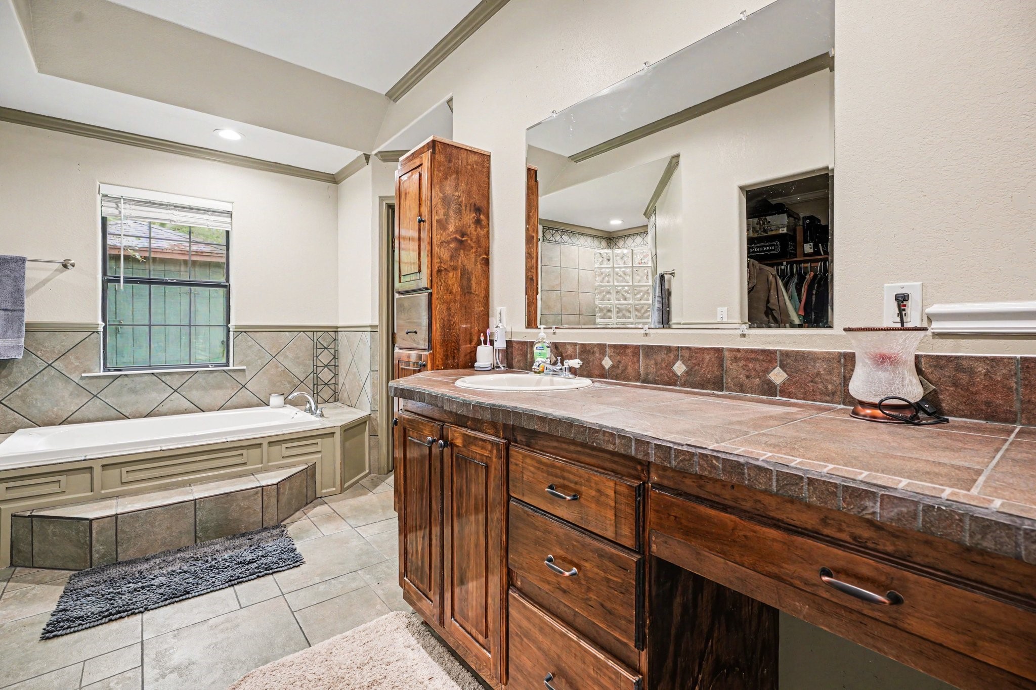 5104 Avenue R Santa Fe, TX 77510 - Photo 20 of 35 This spacious bathroom features a large vanity with ample storage, a tiled countertop, and a wide mirror. It includes a soaking tub with decorative tile accents and a separate shower. The neutral color palette and natural light create a relaxing atmosphere.