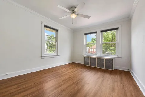 an empty room with wooden floor chandelier fan and windows