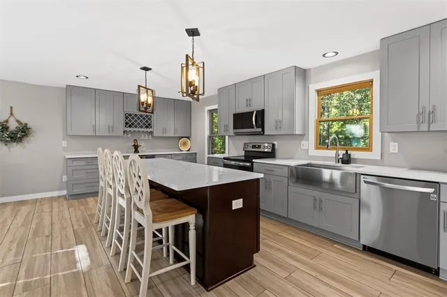 a kitchen with stainless steel appliances granite countertop a sink a stove a refrigerator cabinets and a dining table with wooden floor