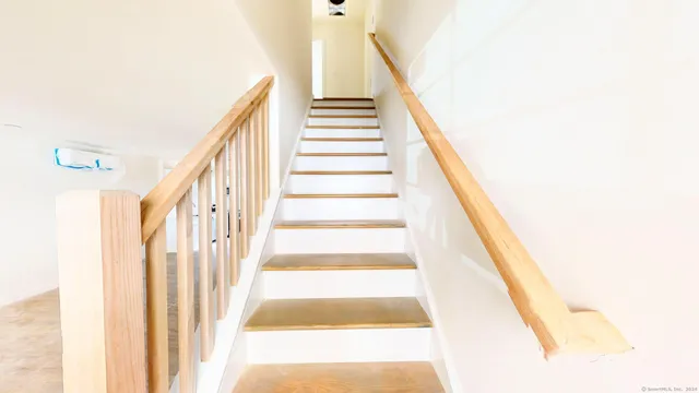 a view of a hallway with wooden floor and a bathroom