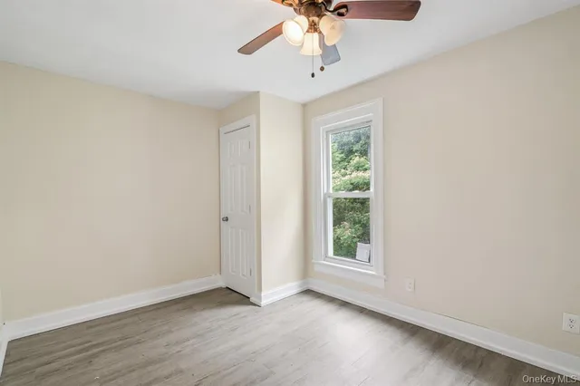 an empty room with wooden floor chandelier fan and windows