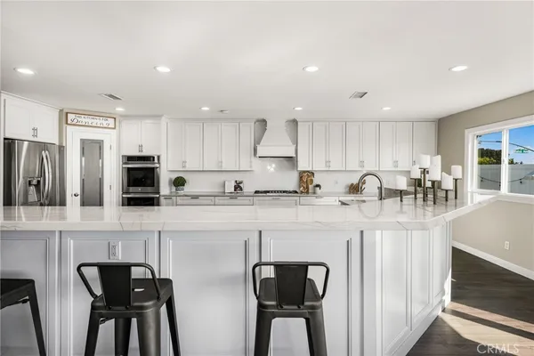 a kitchen with stainless steel appliances granite countertop a stove top oven a refrigerator a sink and a dining table with white cabinets