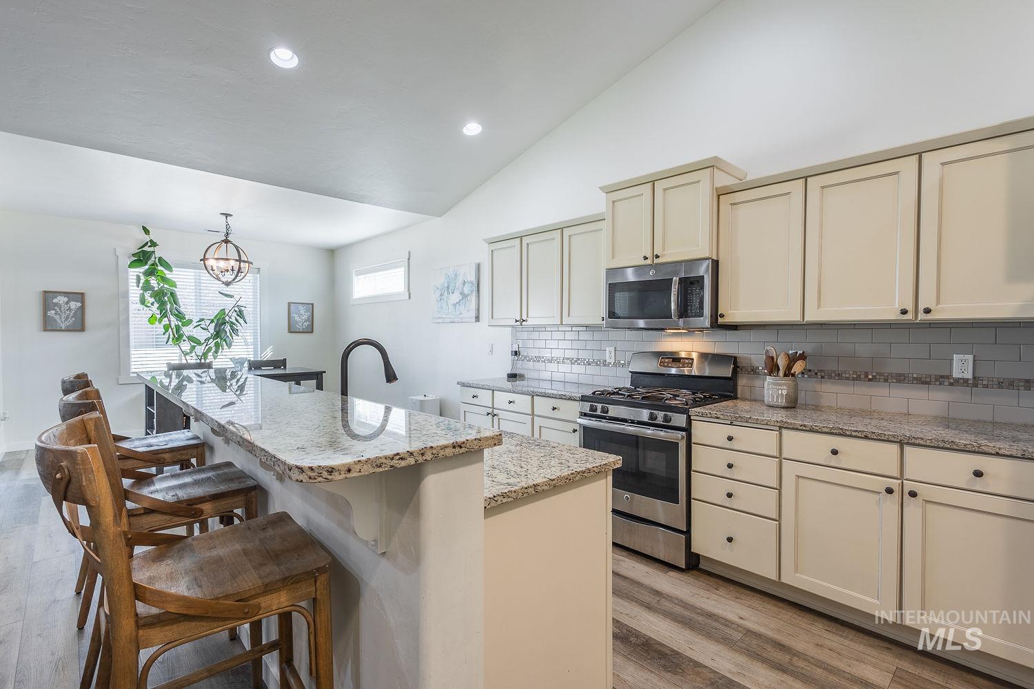 1332 West Raelin Drive Nampa, ID 83686 - Photo 11 of 48 Kitchen with cream cabinets, stainless steel appliances, lofted ceiling, tasteful backsplash, and an island with sink