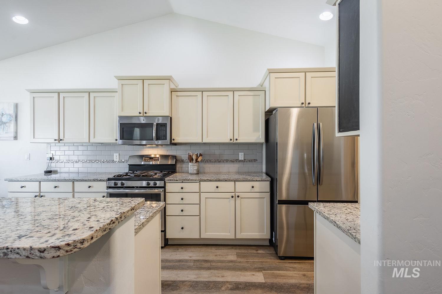1332 West Raelin Drive Nampa, ID 83686 - Photo 13 of 48 Kitchen featuring cream cabinetry, stainless steel appliances, light wood-type flooring, light stone counters, and lofted ceiling
