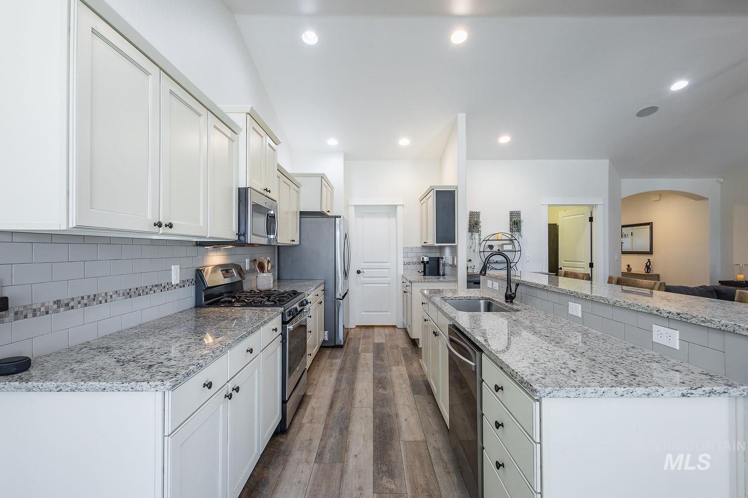 1332 West Raelin Drive Nampa, ID 83686 - Photo 16 of 48 Kitchen featuring stainless steel appliances, light stone counters, dark wood-style flooring, arched walkways, and backsplash