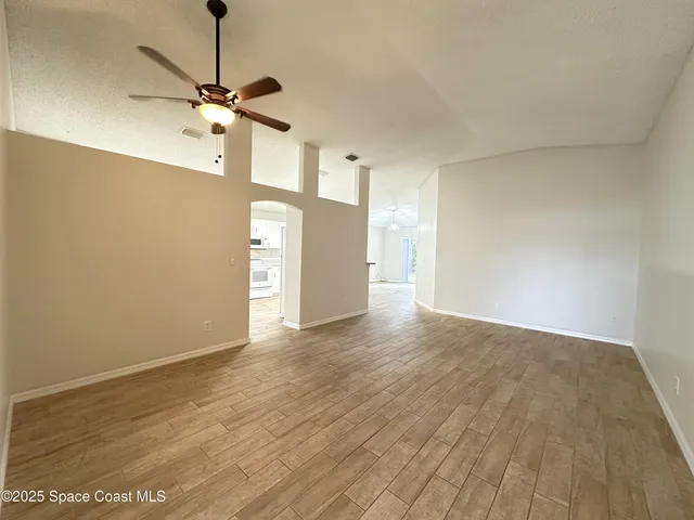 a view of empty room with wooden floor and fan