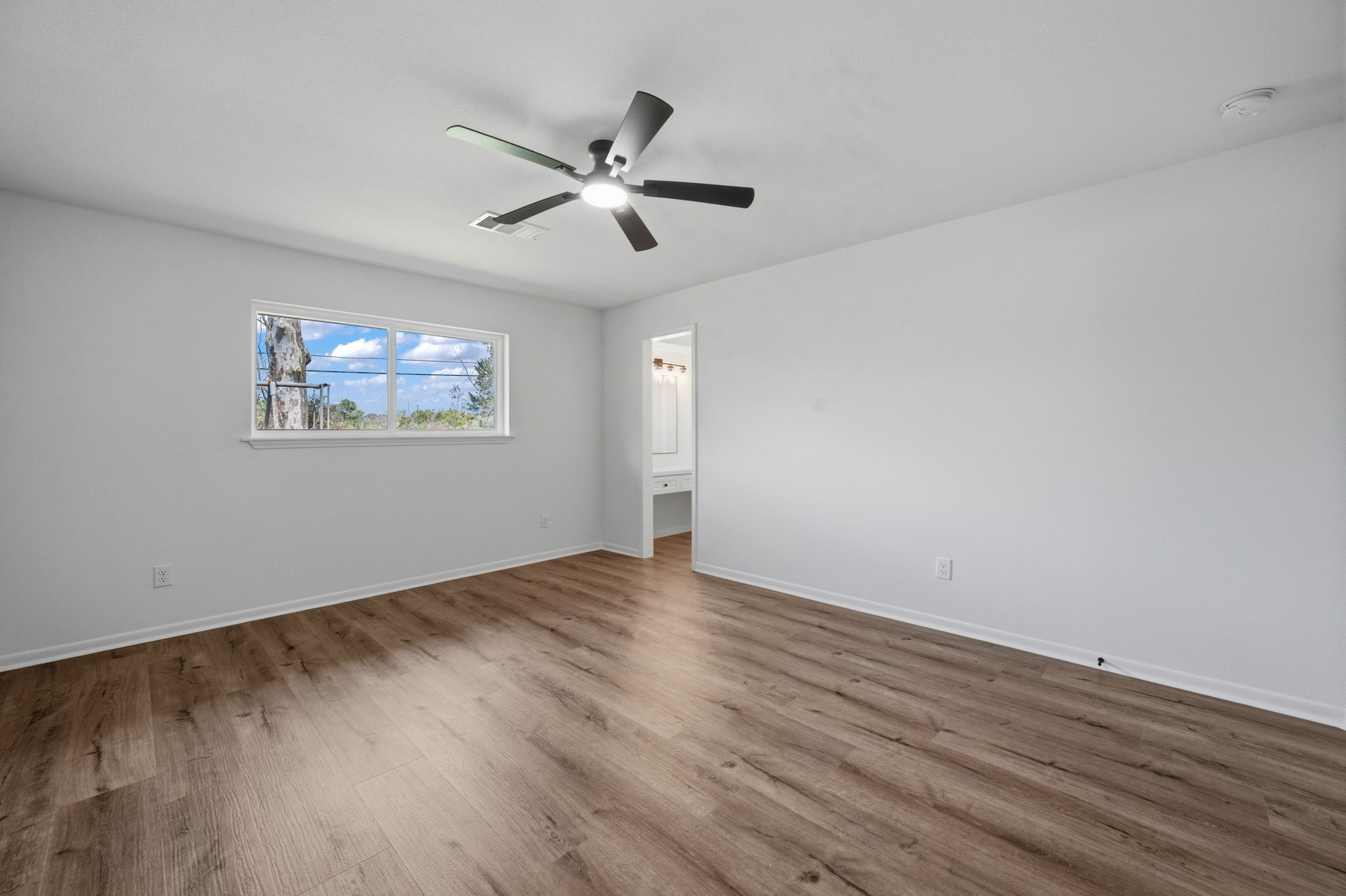 210 Ridgemont Drive Alvin, TX 77511 - Photo 21 of 27 Bright, spacious bedroom with hardwood floors, a modern ceiling fan, and a large window offering natural light and scenic views. There's an open doorway leading to an adjacent area, possibly a bathroom or closet.
