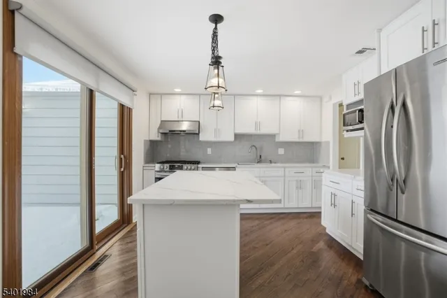 a kitchen with stainless steel appliances granite countertop a refrigerator a sink and white cabinets