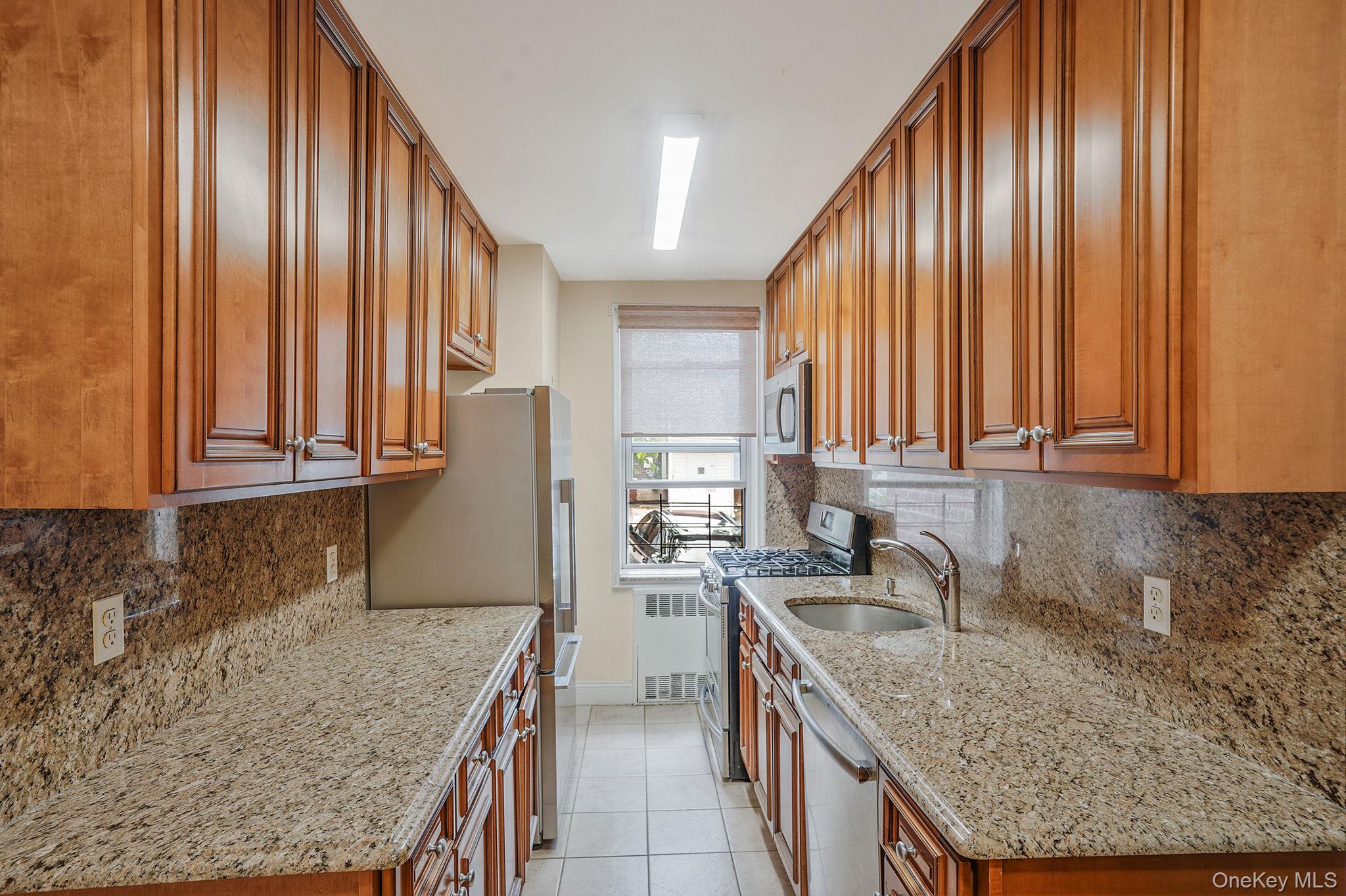 103-26 68th Avenue, Unit 2E Queens, NY 11375 - Photo 12 of 22 Kitchen with stainless steel appliances, a sink, radiator heating unit, brown cabinetry, and light tile patterned flooring