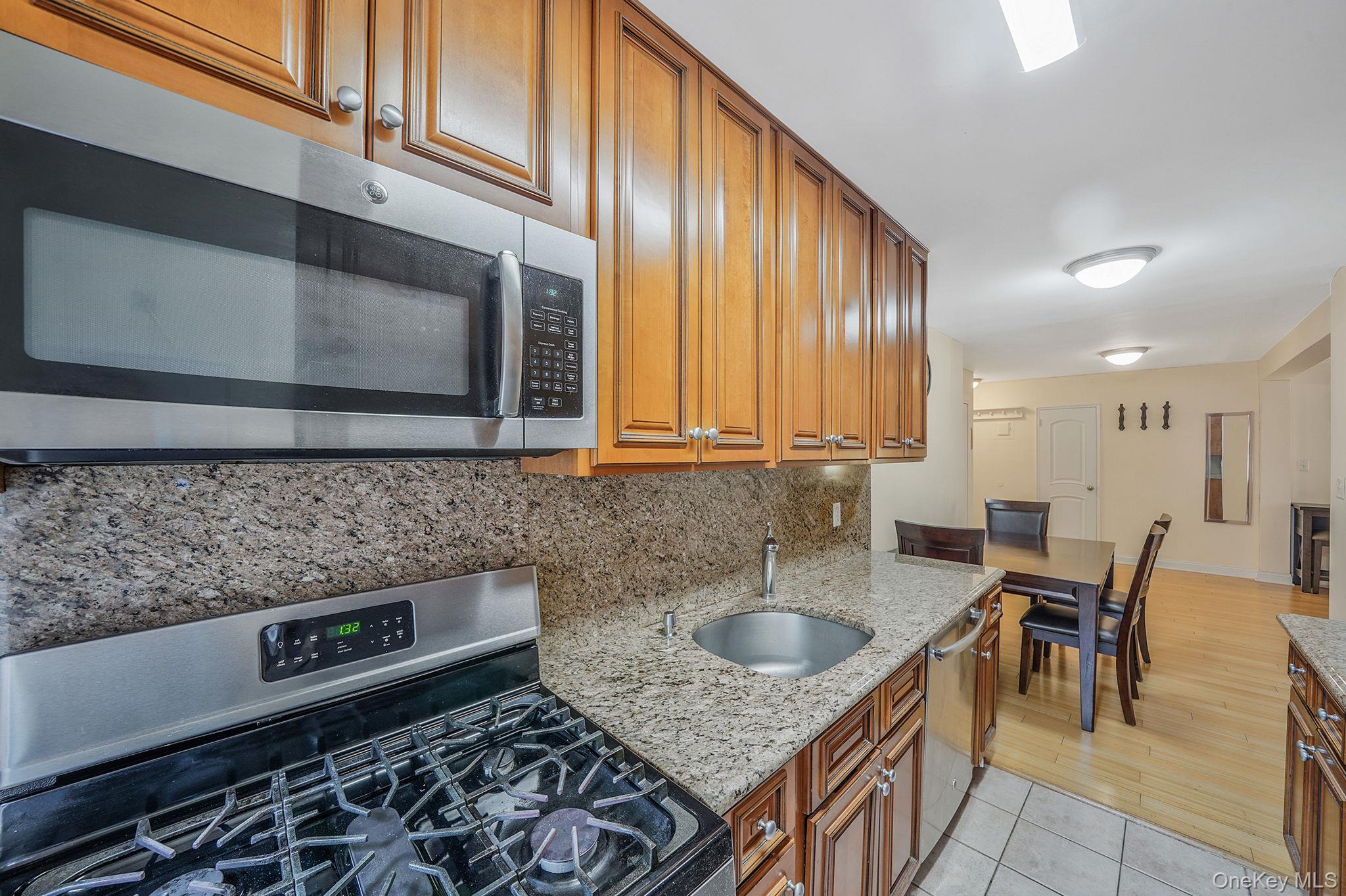103-26 68th Avenue, Unit 2E Queens, NY 11375 - Photo 13 of 22 Kitchen featuring appliances with stainless steel finishes, decorative backsplash, a sink, brown cabinetry, and light stone counters