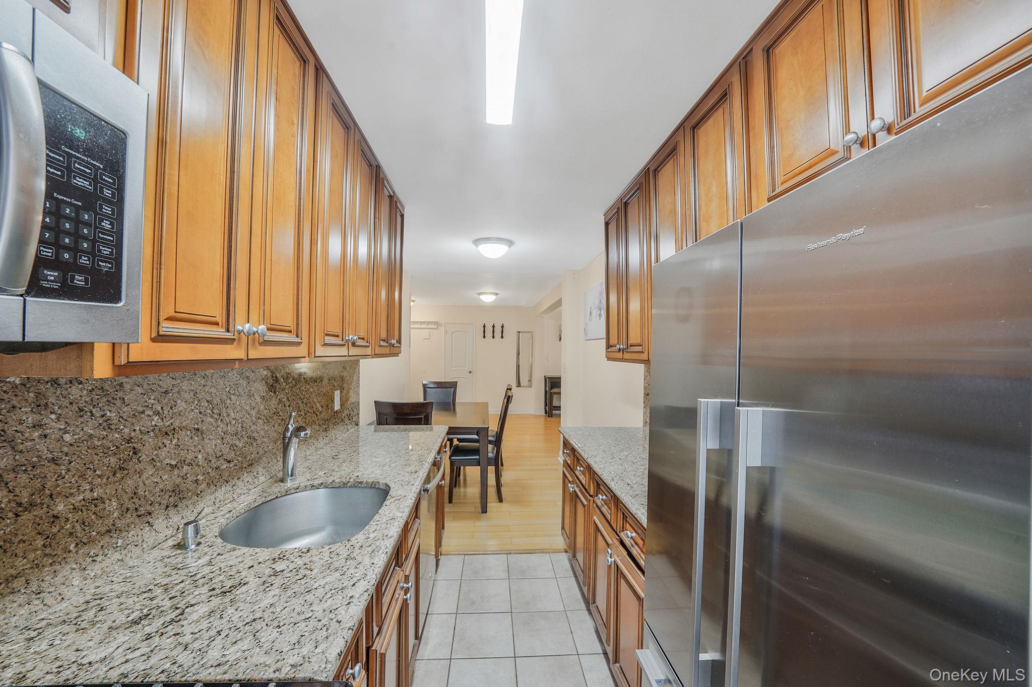 103-26 68th Avenue, Unit 2E Queens, NY 11375 - Photo 14 of 22 Kitchen with stainless steel appliances, a sink, light tile patterned floors, brown cabinetry, and tasteful backsplash